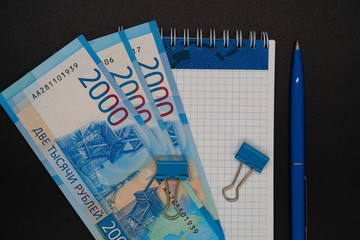 Two thousandth banknotes and blue paper clips on notepad, pen, copywriter