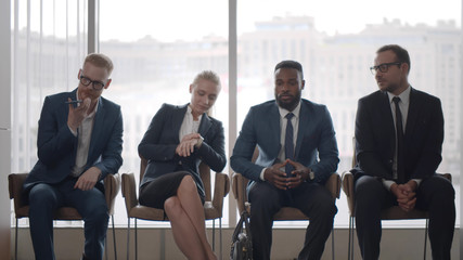 Young candidates waiting for job interview sitting on chairs in reception area