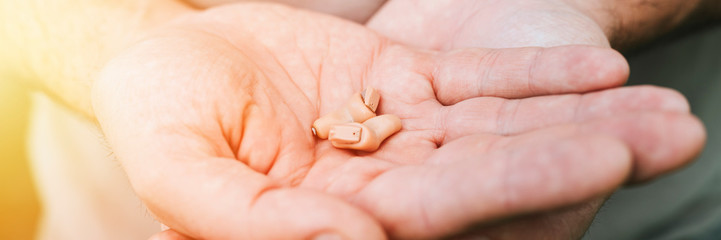 small intra channel hearing aid device in a man's hands. banner. flare