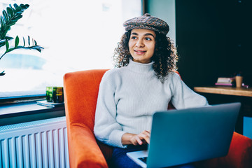 Smiling female copywriter wear in stylish apparel creating publication via netbook spending time at...