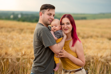 Father, mother and their little son have fun together in a wheat field.