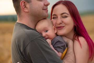 Father, mother and their little son have fun together in a wheat field.