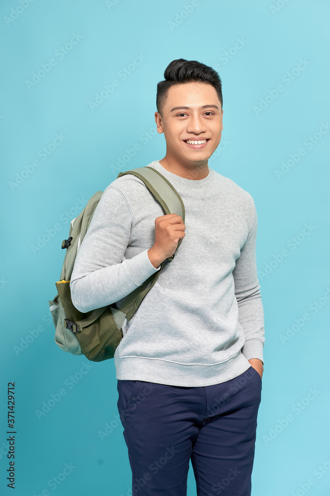 Wall mural handsome casual guy wearing backpack laughing and looking away on blue.