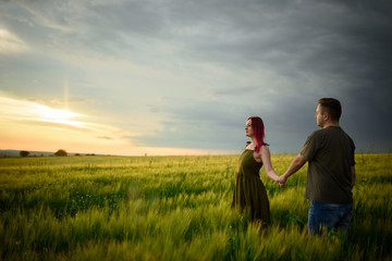 Fototapeta na wymiar Young couple in a wheat field at sunset. Couple spend romantic time together.