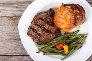 bbq grilled steak dish with green beans and a wrapped bacon potato