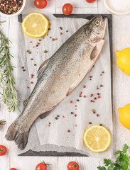 Fresh raw trout with rosemary, cherry tomato, parsley, pepper, salt and lemon. Healthy Mediterranean food and dieting concept, top view, flat lay.
