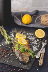 Fototapeta na wymiar Grilled trout with olive oil, rosemary, pepper, salt and lemon placed on the dark background. Healthy Mediterranean food and dieting concept. Served and ready to eat.