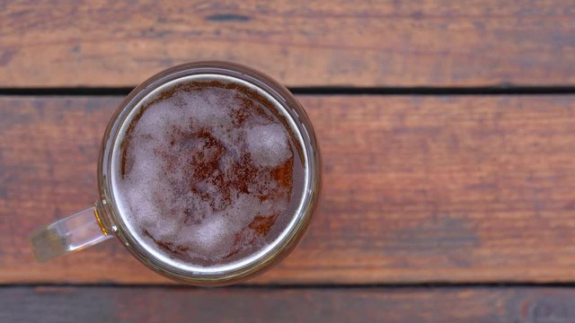 Closeup top view 4k flatlay video of glass pint mug of fresh beer isolated on brown weathered wooden table background.