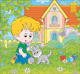 Obraz na płótnie Canvas Little boy playing with a small grey kitten among flowers on green grass of a lawn in front of his house on a sunny summer day, vector cartoon illustration
