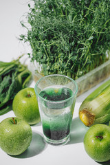 chlorophyll in a glass of water on a white background near are various fresh vegetables fruits and roots with lettuce and spinach