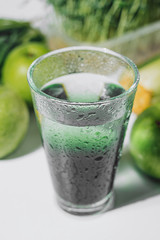 chlorophyll in a glass of water on a white background near are various fresh vegetables fruits and roots with lettuce and spinach