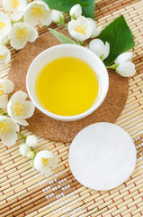 Small white bowl with cosmetic (cleansing, massage) aroma oil, cotton pad and white jasmine flowers. Natural skin care, homemade spa and beauty treatment recipe. Top view, copy space.