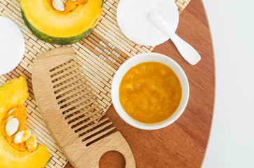 Fresh pumpkin puree in a small white bowl, cotton pad and wooden hair brush. Homemade face mask, natural beauty treatment and spa recipe. Top view, copy space.