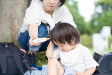 屋外で、非接触型の機器で子供の体温を測る母親