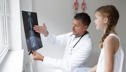 Doctor in white coat examines girl's back and shows X-ray in hospital