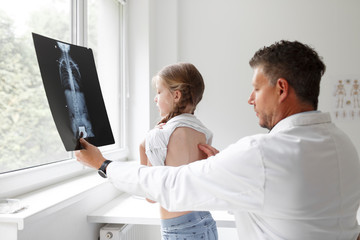 Doctor in white coat examines girl's back and shows X-ray in hospital