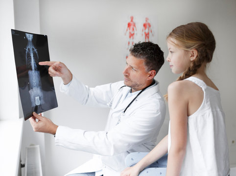 Doctor in white coat examines girl's back and shows X-ray in hospital