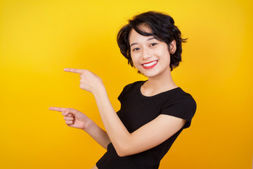 Positive attractive young female, points aside with cheerful and surprised expression with mouth opened, shows something amazing standing indoors. Advertisement concept.