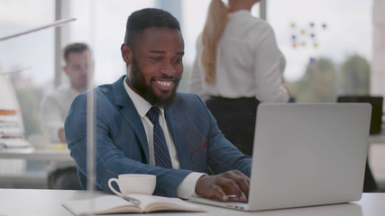 Secretary bringing coffee to young african businessman working on laptop