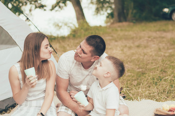 Family sitting on the background of the tent, eating cookies, drinking tea and fooling around