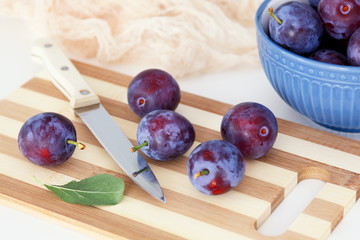 Plums lying on a cutting board with a kitchen knife