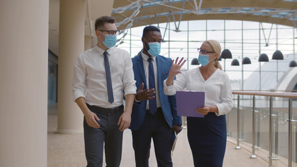 Business team wearing protective masks walking in modern office corridor