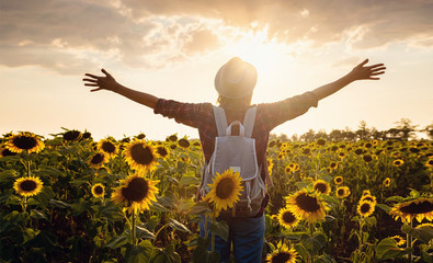 Beautiful young woman enjoying nature on the field of sunflowers at sunset