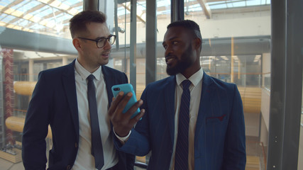 Businessman smiling communicating with colleague in elevator using smartphone
