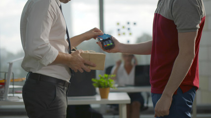 Side view of employee receiving parcel in office paying with credit card for delivery