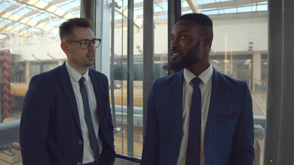 Young diverse colleagues smiling and chatting lifting in glass elevator