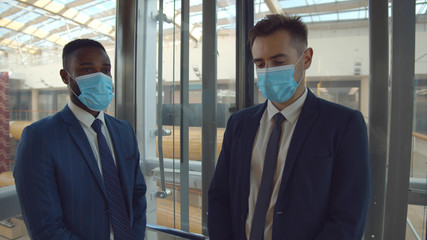 Diverse employees in safety mask taking glass elevator in business center