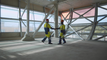 Side view of diverse foreman and engineer shaking hands while standing on construction site