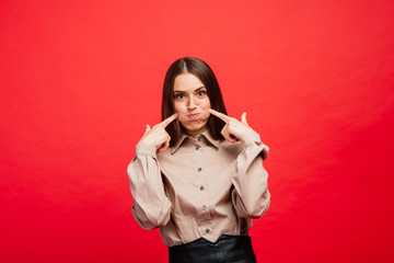 Fototapeta premium What is it. The female portrait isolated on red studio backgroud. The young emotional angry, scared woman looking at camera.The human emotions, facial expression concept.