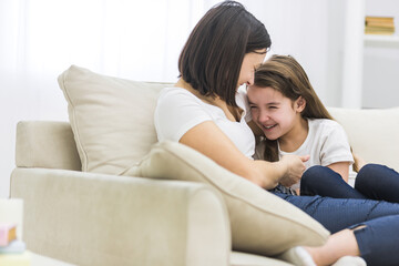 Photo of happy mother and daughter talking on sofa in living room.