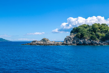 Fototapeta premium Beautiful landscape - sea lagoon with turquoise water, stones and rocks, blue sky with clouds and mountains on the horizon. Corfu Island, Greece.