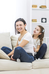 Photo of smiling mother and daughter on the sofa.