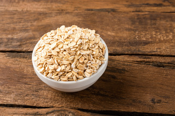 Rolled oats in bowl on vintage wooden background
