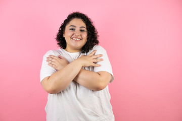 Young beautiful woman standing over isolated pink background hugging oneself happy and positive, smiling confident