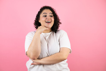 Young beautiful woman standing over isolated pink background looking side confident, smiling with crossed arms and hand raised on chin