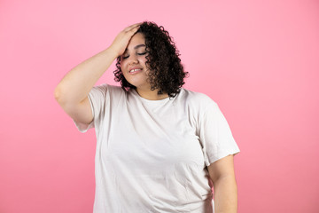 Young pretty woman putting one hand on her head smiling like she had forgotten something standing on pink background.