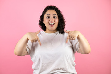 Young beautiful woman over isolated pink background surprised and pointing down with fingers and raised arms