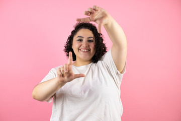 Young beautiful woman standing over isolated pink background smiling making frame with hands and fingers with happy face