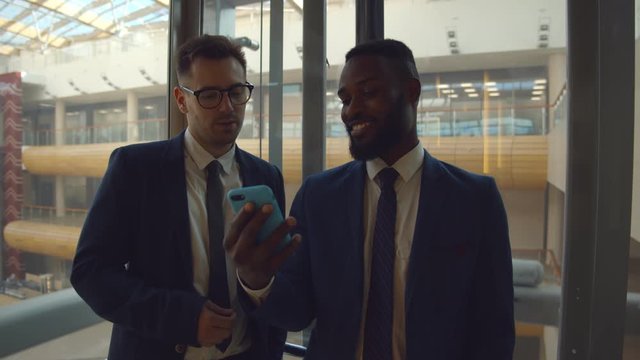 Businessman smiling communicating with colleague in elevator using smartphone