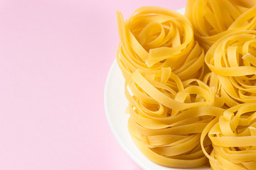 nest of pasta on a pink background. Italian pasta. The pasta nests are on a white plate. European cuisine