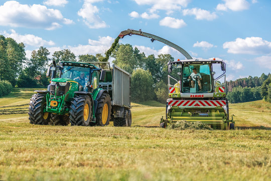 BAVARIA / GERMANY - AUGUST 07,2020: Claas Jaguar 930 harvester and a John Deere 6175R with a Fliegl Gigant trailer works on a field.