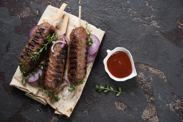 Barbecued lula kebabs with lavash flatbread and dip sauce, above view on a brown stone background,...