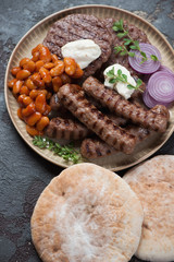 Serbian traditional grilled cevapi sausages and pljeskavicas with kajmak, prebranac and pita, selective focus, vertical shot