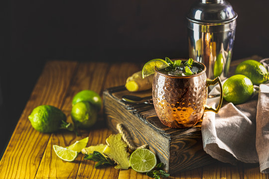 Moscow mule alcoholic cocktail in copper mug with crushed ice, mint and lemon over minton dark wooden table with amazing backlight, copy space. Close up view, copy space