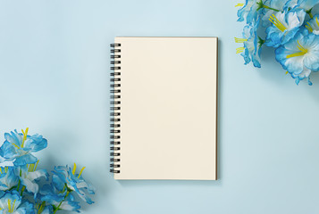 Spiral Notebook or Spring Notebook in Unlined Type and Blue Flowers at Bottom Left and Top Right Corner on Blue Pastel Minimalist Background. Spiral Notebook Mockup on Center Frame