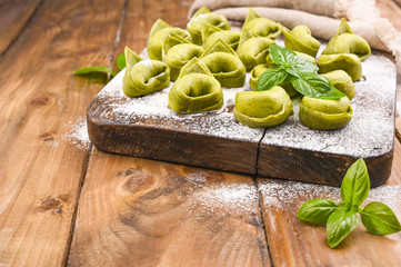 Tortellini e tortelloni typical dishes emilia italy. Food background with homemade raw Italian tortelloni and ingredients for green pesto on wooden background . High angle view. Copy space.
